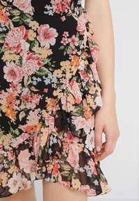 Robe florale avec un fond noir, présentant de grandes fleurs roses et jaunes, des volants sur le côté, et un tissu léger et texturé.