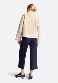 Jachetă din blană artificială bej cu guler înalt, asortată cu pantaloni evazați bleumarin și adidași bleumarin cu accente argintii.