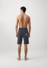 Shorts de bain pour hommes gris foncé avec un motif uni, ceinture élastique et détail de logo sur la poche arrière. Fabriqués en tissu léger.