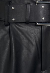 Falda de cuero negra con un acabado texturizado, que cuenta con un cinturón ancho con herrajes plateados y un detalle elegante de hebilla metálica.