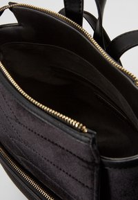 Czarna torebka z tkaniny o gładkiej fakturze, zapięcie na złoty zamek i kieszeniami wewnętrznymi. Posiada podwójne uchwyty i usztywnioną konstrukcję.