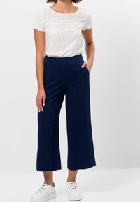 Vit ärmlös blus med en texturerad spetsinlägg, ihopparad med marinblå vida byxor och vita sneakers. Minimalistisk design och avslappnad passform.