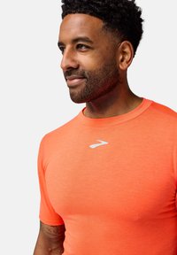 Camiseta deportiva de manga corta en un vibrante color naranja con una textura suave. Presenta un pequeño logotipo blanco en el pecho y un cuello redondo.