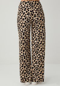Beige wijde broek met luipaardprint en zwarte vlekken, met een gladde textuur en een hoge taille. Einde bij de enkels, gecombineerd met witte schoenen.