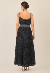 Langes schwarzes Kleid mit floralem Muster, Spaghettiträgern, tailliertem Schnitt und einem schwingenden Rock, kombiniert mit silbernen High Heels.