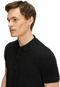Czarna koszulka polo z krótkim rękawem, z trzema guzikami, żebrowanym kołnierzykiem i fakturowanym materiałem. Zaprojektowana, aby dopasować się do sylwetki.