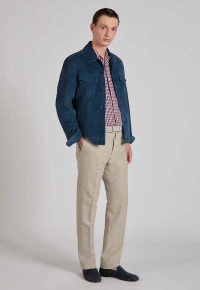 Veste en daim bleu avec deux poches poitrine, chemise à carreaux rouges et blancs, pantalon en lin beige, et chaussures sans lacets bleu foncé.