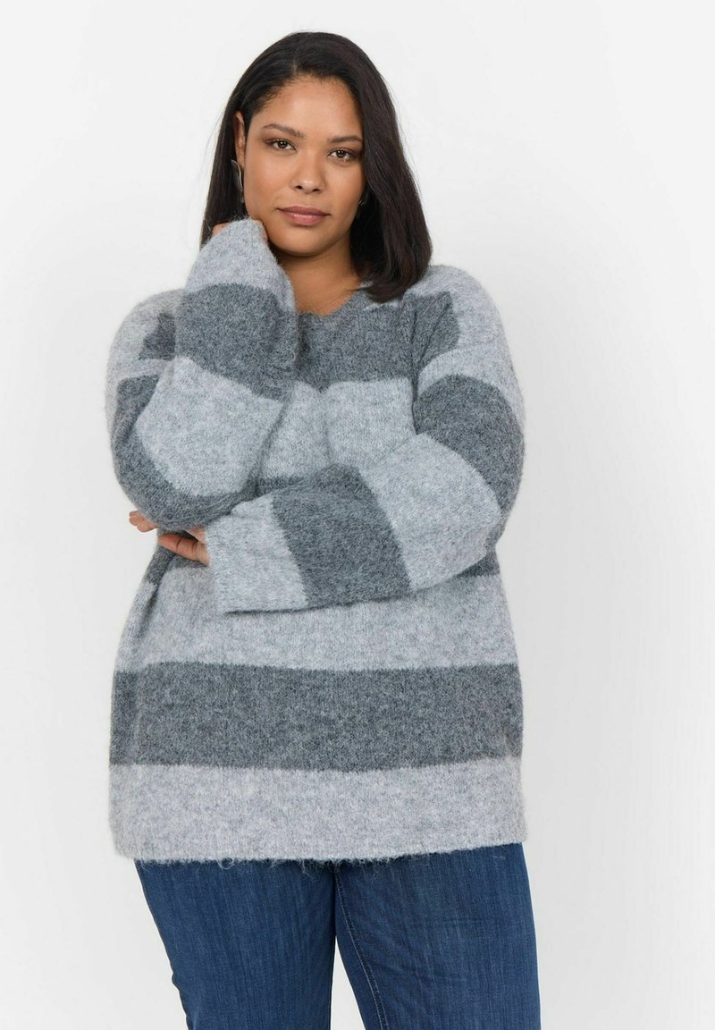 Pull rayé gris et gris clair, fabriqué en matière douce et moelleuse. Col rond, épaules tombantes et coupe décontractée. Associé à un jean en denim foncé.