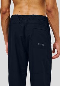 Granatowe, lekkie spodnie z elastycznym paskiem w pasie i strukturą rib. Posiadają tylnią kieszeń z etykietą "B-583".