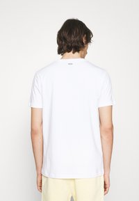 Tricou alb cu mânecă scurtă, cu guler rotund și etichetă "HUGO" pe spate. Fabricat dintr-un material neted, cu un croi lejer.