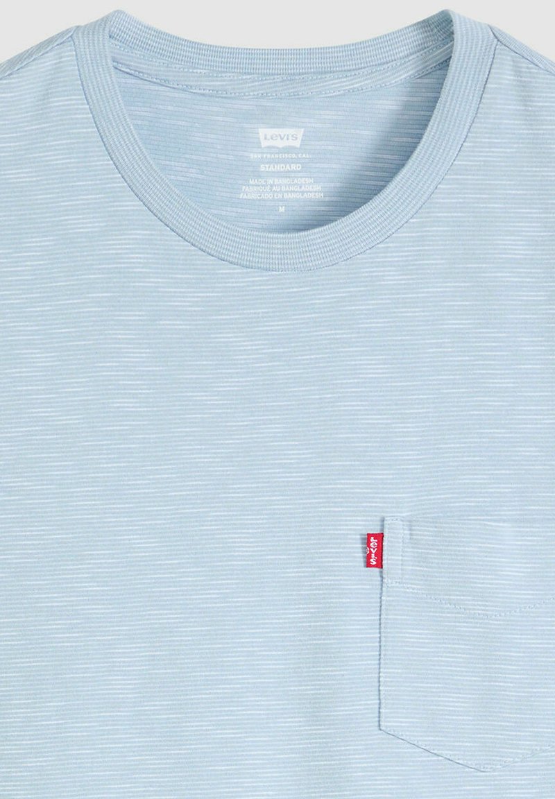 Maglietta a righe sottili azzurro chiaro e bianco con una piccola tasca sul petto a sinistra e una targhetta con il logo Levi's rossa.