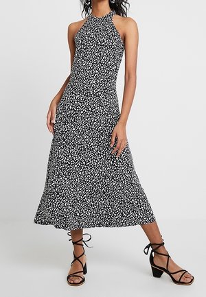 Femme portant une robe midi noire et blanche sans manches à col licou avec un motif abstrait et des sandales à talons carrés noirs lacées.