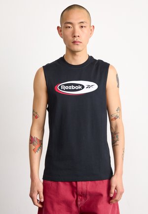 Juodas be rankovių medvilninis marškinėliai su centrinio balto Reebok logotipo raudonu kontūru, dėvimi su raudonomis šortais, matomi tatuiruotės ant rankų.
