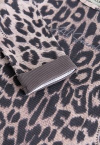 Leopardprint stof med en ribbet tekstur. Beklædningen har en grå manchet med en hvid inderside og subtile broderede detaljer.