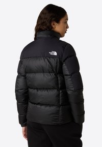 Svart dunjakke med høy krage, quiltet design og logo på den øvre ryggen. Laget av vannavstøtende materiale med elastiske mansjetter.