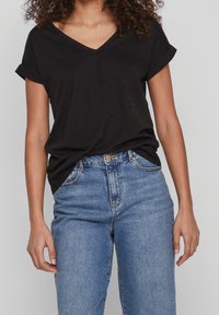 Černé bavlněné tričko s výstřihem do V a krátkými rukávy s ohrnutím, spárované s modrými džínami s vysokým pasem. Jednoduchý design, jemná textura.