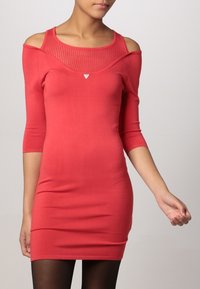 Rode bodycon jurk met schouderuitsparingen en een gestructureerd bovenstuk. Beschikt over een driehoekige accent boven de buste. Lange mouwen, aansluitende silhouet.