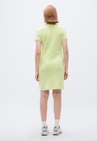 Robe vert clair à manches courtes avec une coupe ajustée. Tissu en coton lisse, longueur genou, avec un col classique. Portée avec des baskets.