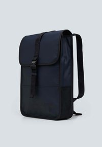 Zaino blu navy con chiusura a patta, spallacci neri regolabili, tasca anteriore e marchio in rilievo nella parte inferiore. Texture liscia.