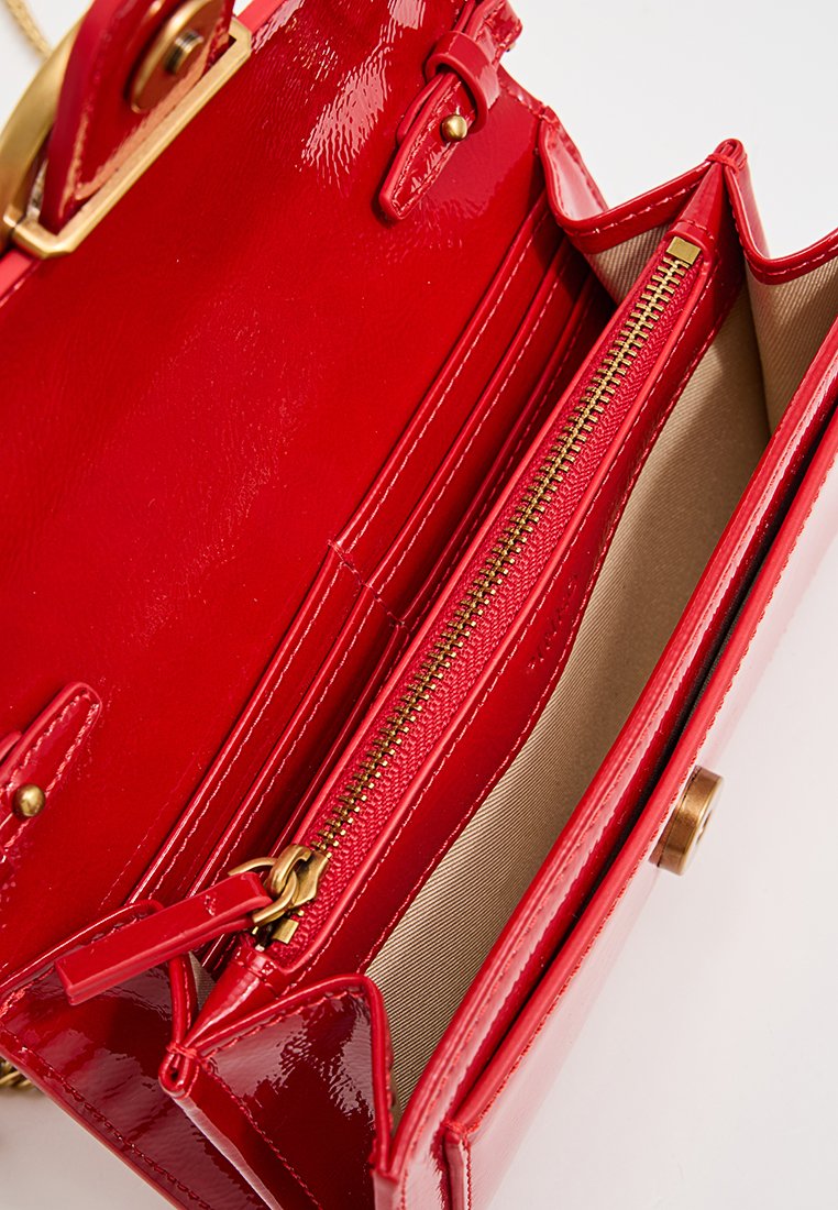 Czerwona torebka z lakierowanej skóry z złotymi elementami, z jedną kieszenią na zamek i beżową podszewką, charakteryzująca się usztywnioną konstrukcją.