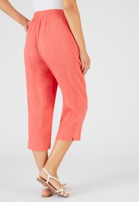 Pantaloni culotte corallo con texture plissettata e vita elastica, dotati di fessure laterali all'orlo e abbinati a sandali di colore chiaro.