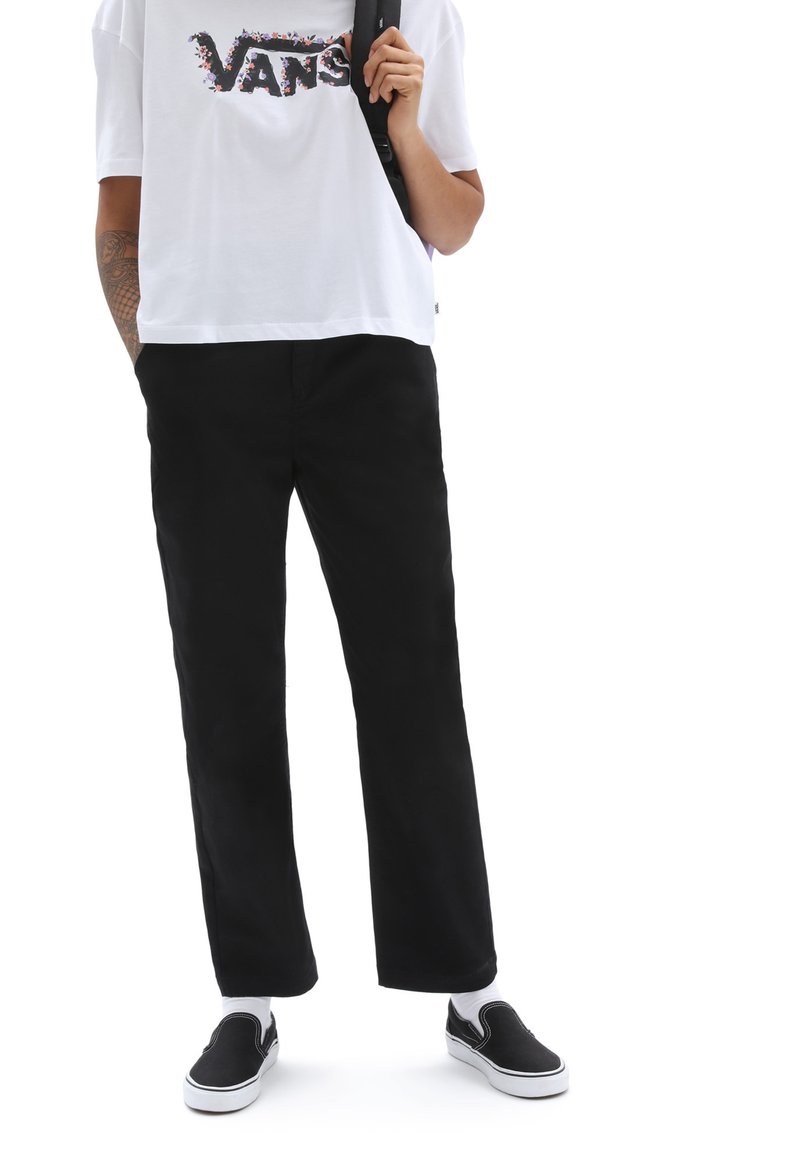 Sorte bukser med lige pasform, parret med en løs hvid t-shirt med et flerfarvet "VANS" logo og sorte slip-on sko.