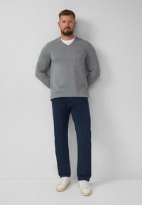 Grijze v-hals trui, marineblauwe broek en witte sneakers. De trui is gemaakt van zacht materiaal en de broek heeft een slim fit ontwerp.