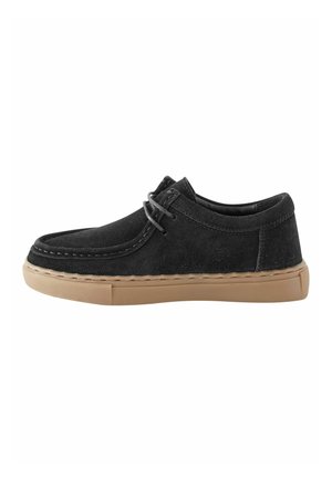 Sort ruskind afslappet sko med moc toe-design, beige gummisål og matchende sorte snørebånd, vist fra siden på hvid baggrund.