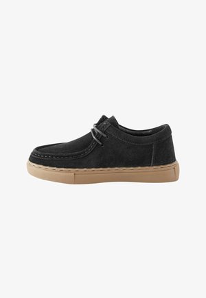 Sort ruskind afslappet sko med moc toe-design, beige gummisål og matchende sorte snørebånd, vist fra siden på hvid baggrund.