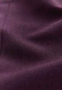 Textilstoff in tiefem Violett mit einer glatten, leicht strukturierten Oberfläche, die feine Webdetails und subtile Schattierungsvariationen zeigt.