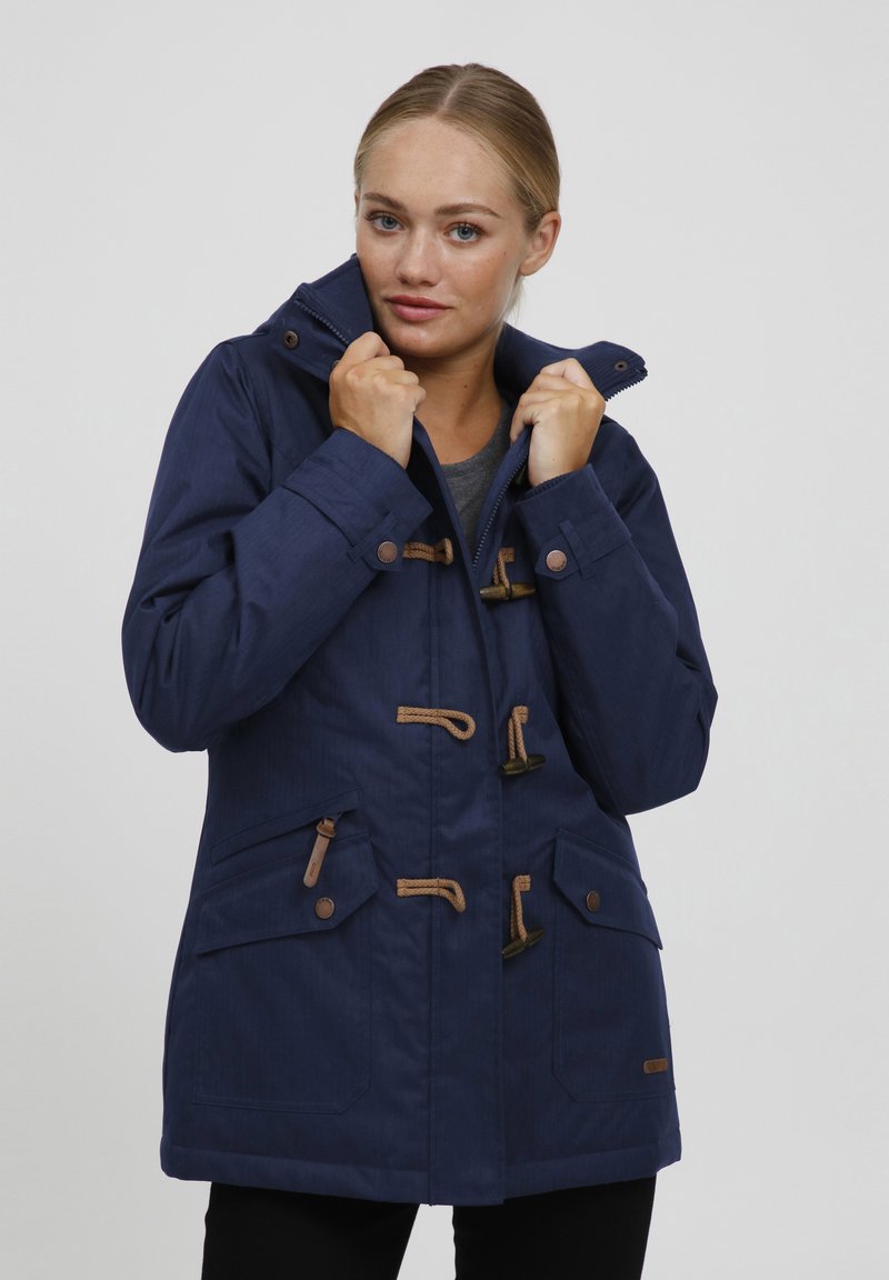 Veste imperméable bleu marine avec fermetures à toggles, une capuche et plusieurs poches, dotée d'un tissu texturé et d'accents bruns contrastants.