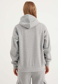 Grauer Kapuzenpullover mit lockerer Passform, gerippten Bündchen und Saum. Schlichte Textur, minimalistisches Design und leicht übergroße Ärmel.