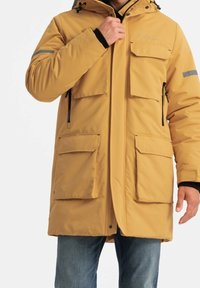 Parka aislante amarilla con capucha, cuatro bolsillos frontales y bolsillos laterales con cremallera. Cuenta con puños elásticos y detalles reflectantes.