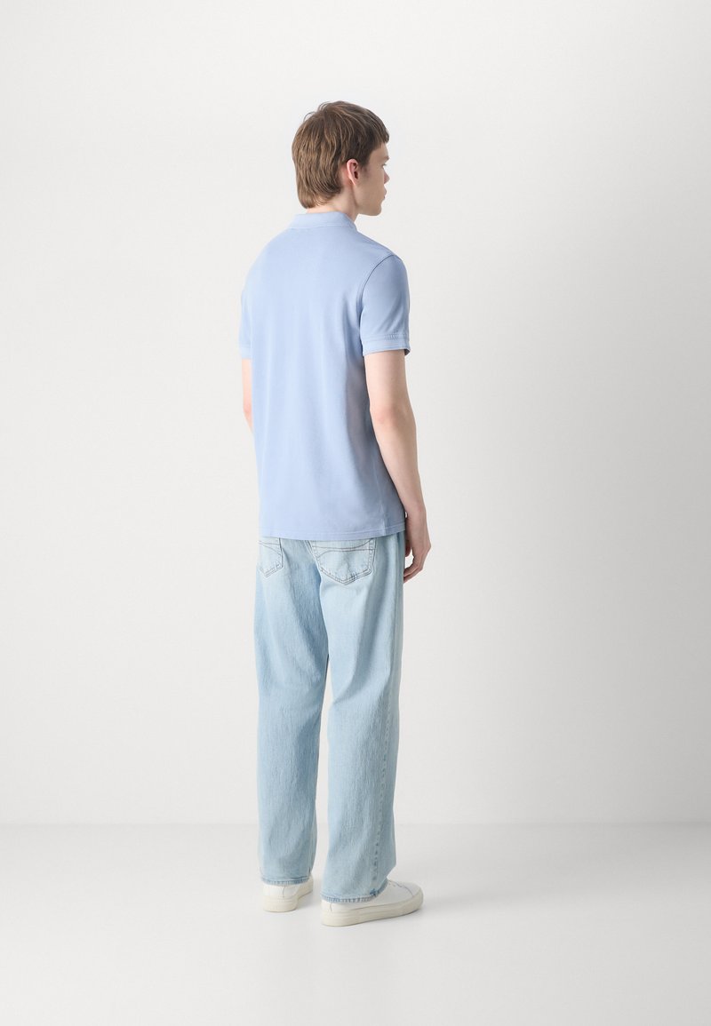 Polo shirt bleu clair à manches courtes, accompagné d'un jean en denim léger à coupe ample et de baskets blanches, vu de dos.