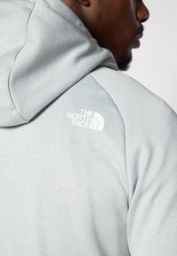 Light gray hooded sweatshirt featuring a soft texture, raglan sleeves, and a white printed logo on the upper back.