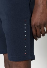 Shorts en coton bleu marine avec une coupe ajustée, arborant un texte logo vertical en lettres multicolores sur le côté. Texture lisse.