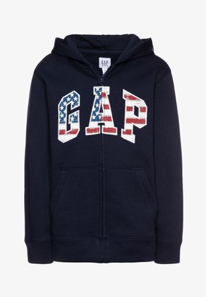 Sweat à capuche à fermeture éclair pour enfants de couleur bleu marine avec poches avant et logo GAP affichant un design d'étoiles et de rayures du drapeau américain sur la poitrine.