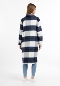 Cappotto lungo a quadri in blu navy e bianco, realizzato in tessuto morbido. Presenta un colletto, polsini con bottoni e un design con schiena aperta.