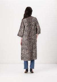 Cappotto lungo a stampa leopardata con maniche a tre quarti, realizzato in un tessuto liscio; indossato sopra un paio di jeans e scarpe con tacco, visto da dietro.