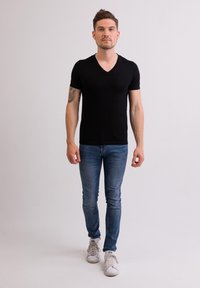 Černé tričko s výstřihem do V z měkké látky, v kombinaci s modrými džíny a bílými teniskami, úzkého střihu a krátkými rukávy. Minimalistický design.