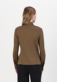 Brown long-sleeve shirt with a structured collar, fitted design, and buttoned cuffs. Smooth, lightweight fabric with no visible patterns.