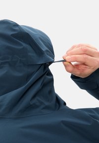 Giubbotto impermeabile blu con cappuccio, dotato di coulisse regolabile. Tessuto liscio con pieghe vicino al colletto per la regolazione della vestibilità.