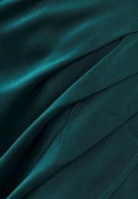 Teal satin tyg med en mjuk textur, som visar mjuka draperingar och en subtil lyster, vikt prydligt med synliga sömnadsdetaljer.