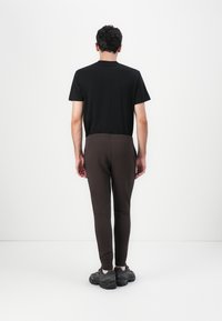 Schwarzes T-Shirt mit kurzen Ärmeln, braune schlanke Jogginghosen mit elastischem Bund und dunkle Sportschuhe. Schlichtes Design, Baumwollmaterial, minimalistische Details.