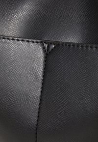 Svart läderhandväska med en strukturerad yta, med en sydd söm och en slät, polerad sektion. Ingen ytterligare hårdvara eller mönster.