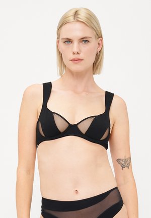Zwarte bh met doorzichtige netpanelen, gevormde cups, brede banden en een gladde stofafwerking. Het design heeft een laag uitgesneden silhouet.