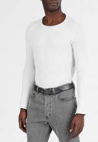 Camisa blanca de manga larga de canalé, con un diseño ajustado. Combina con jeans grises y un cinturón negro. La textura muestra un fino canalé y un cuello redondo.