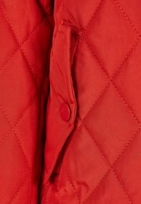 Röd quiltad jacka i tyg med diamantmönster. Har en sidoficka och en matchande röd tryckknapp. Mjuk textur och lätt material.
