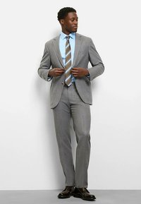 Gray tailored suit with a light blue dress shirt and a brown striped tie. Worn with brown dress shoes and intricate detailing on the suit.