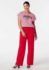 T-shirt rayé rouge et blanc avec un graphique "PARIS", associé à un pantalon rouge taille haute avec des coutures latérales et des sandales à talons blocs bleues.